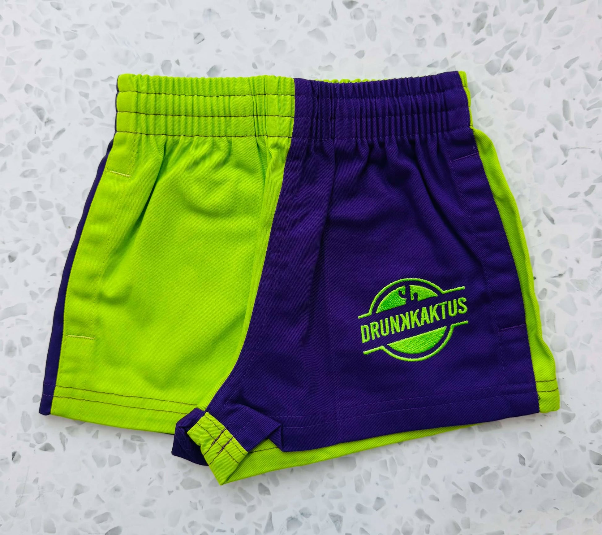 Close-up of kids green purple ruggers cotton drill shorts showcasing the two-tone fabric texture and stitching details.