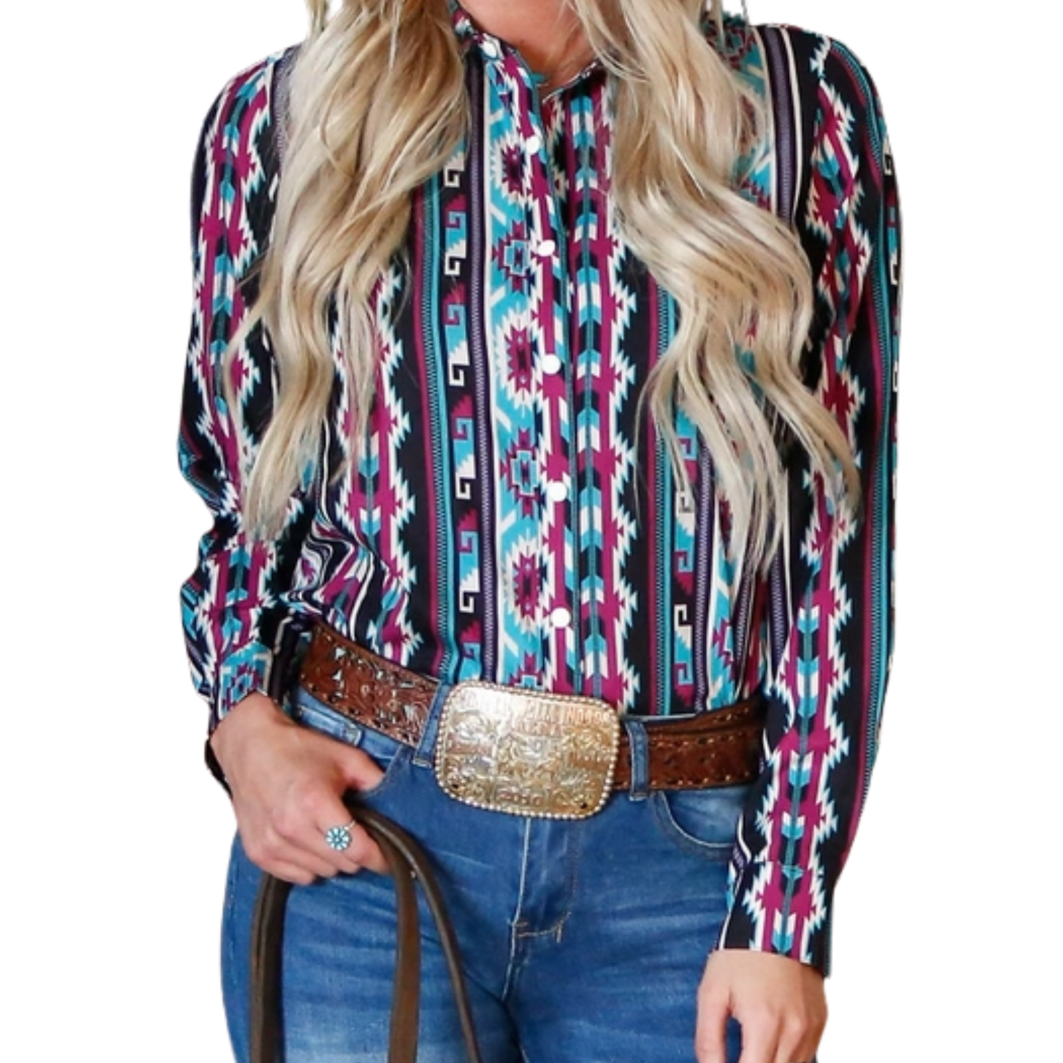 A woman wearing a long-sleeved Western-style button-up top with a vibrant turquoise and purple Aztec pattern, tucked into blue jeans with a wide brown belt and a large gold rodeo-style buckle, holding a leather strap.